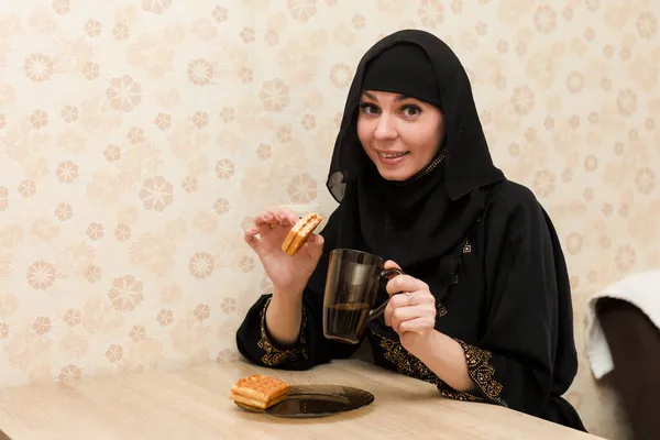 国民服のイスラム教徒の女性は キッチンテーブルでお茶とクッキーと朝食を持っています — ストック写真