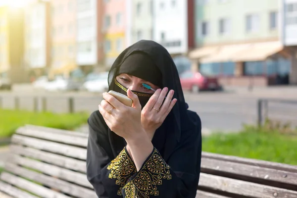 イスラム教徒の女性で国民服でベンチに市公園で彼女のまつげをペイント彼女の鏡を見て — ストック写真