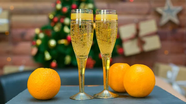 Två Glas Champagne Och Ljusa Saftiga Apelsiner Bakgrunden Elegant Julgran — Stockfoto