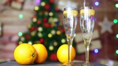 Şampanya, parlak portakalların ve Noel ağacının arka planına karşı güzel bir şarap bardağına dökülür.