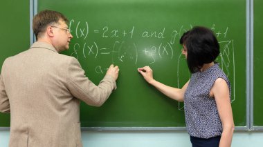 Tahtadaki yetişkin bir öğretmen, öğrencisine matematik probleminin çözümünü açıklar..