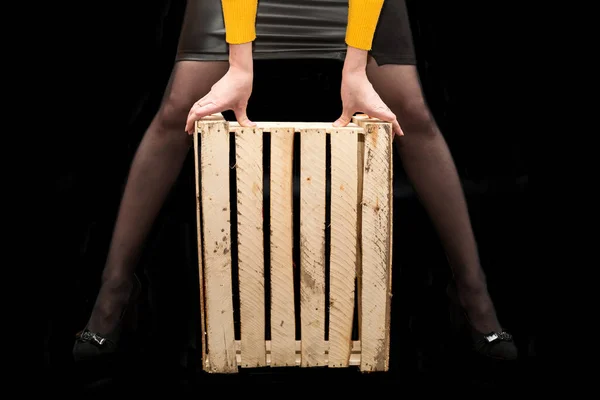 女人的手在她们的两腿之间拿着一个木制的盒子 底色是黑色的 — 图库照片