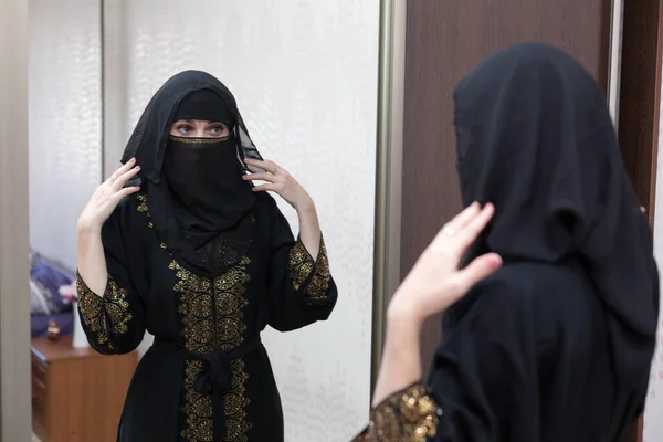 一位穆斯林妇女在公寓的前视镜前穿衣 调整她的罩袍 — 图库照片