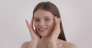 Güzel surat. Doğal güzelliği olan çekici genç bir kadın parmaklarıyla yüz masajı yapıyor. Beyaz kadın modelin sağlıklı ve taze bir teni var. Güzellik rutini kavramı.