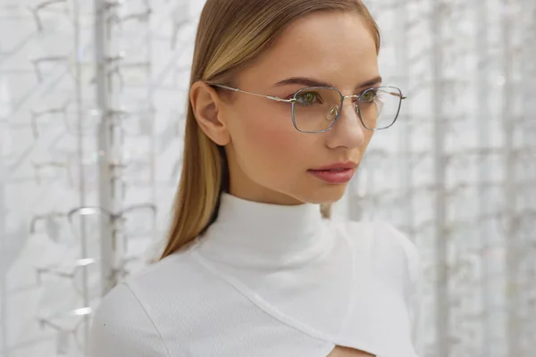 眼镜店的女顾客的肖像 布隆德时装模特戴着时髦的光学眼镜 背对着装有玻璃的展示柜 — 图库照片