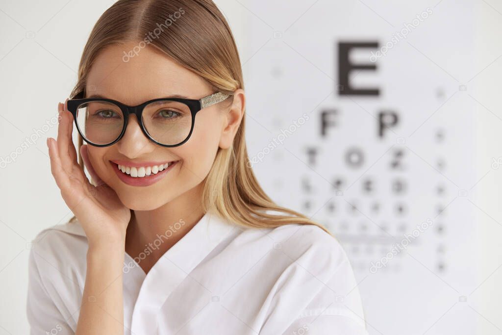 Optometry And Vision. Smiling Girl At Ophthalmologist Office. Portrait Of Beautiful Woman Face With Healthy Eyes And Visual Eye Test Chart On Background. High Resolution Image