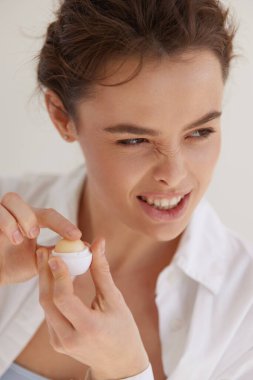 Dudaklar önemser. Kolajen dudak kremi tutan ve gri stüdyo geçmişine bakan yaramaz genç bir kadın. Kadın güzelliği ve kozmetik konsepti. 