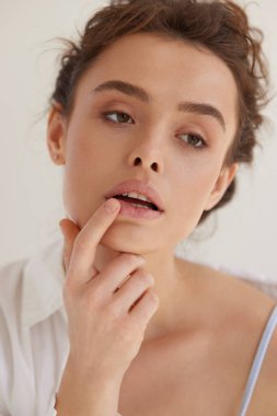 Dudaklar önemser. Stüdyoda seksi dudaklarında parmaklarıyla şehvetli pozlar veren muhteşem genç bir kadın. Gri arkaplanda doğal makyajlı beyaz saçlı bir model..