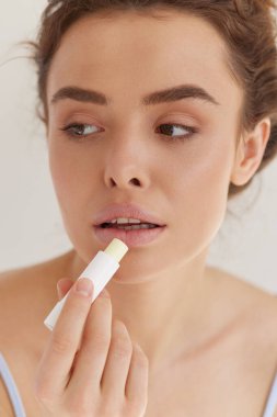 Dudaklar önemser. Dudaklarını nemlendirmek ve dudaklarını korumak için ruj süren kahverengi saçlı güzel bir kadın. Güzellik rutini ve kozmetik konsepti.