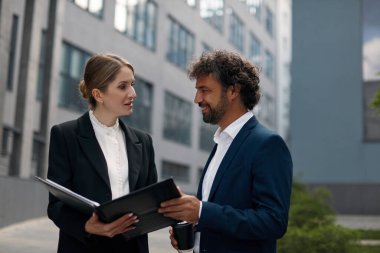 Business Couple Outdoors Examining Documents. Attractive Businessman and Businesswoman Standing with Paperwork at Urban Street. Young People Discussing Project Outside 