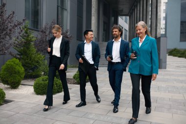 Business People Going From Work to Break. Four White Collar Workers in Formal Wear Walking Along the Street During the Break at Office, Urban Background. Brainstorming or Discussing Project 