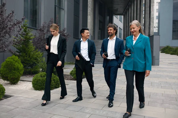 Business People Going From Work to Break. Four White Collar Workers in Formal Wear Walking Along the Street During the Break at Office, Urban Background. Brainstorming or Discussing Project