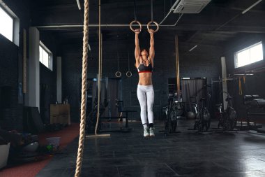 Female Athlete Performing Pull-ups on Gymnastic Rings. Fitness and Woman with Strong Beautiful Body Exercising on Gym Rings. Health and Power Concept 