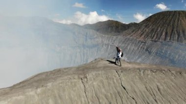 Couple Hugging on Ridge of Mount Gunung Bromo Volcano. Happy Woman Waving to Camera. Concept of Adventure and Travelling. East Java, Indonesia