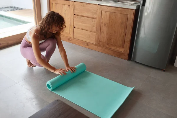 Exercise At Home. Woman Rolling Yoga Mat After Practicing. Female In Sportswear Folding Fitness Rug After Completing Daily Sport Routine. Staying Active And Fit During Social Isolation