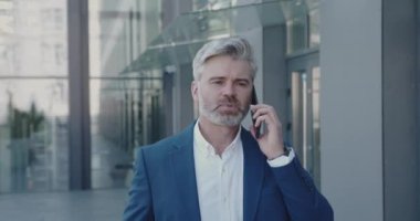 İş adamı, tatilde akıllı telefonu açık tutuyor. Kıdemli İşadamı Gezici Gezgin Sokakta Konuşuyor. Olgun Adam Ofis Binası 'nın yanındaki iş arkadaşına seslendi. İş ve Yaşam Tarzı Konsepti 