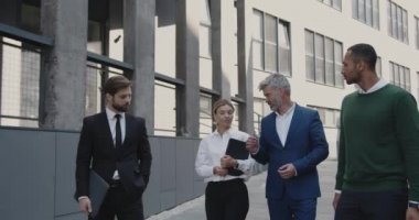 Business People Going From Work to Break. Four White Collar Workers in Formal Wear Walking Along the Street During the Break at Office, Urban Background. Brainstorming or Discussing Project 