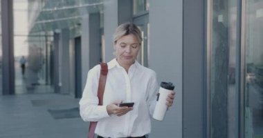 İşe gitmek için elinde kahve tutan iş adamı. Kıdemli iş kadını sokakta hızlı gidiyor. Olgun Kadın İçecek Tutucu Ofis Binası 'nın yanında. İş ve Yaşam Tarzı Konsepti 