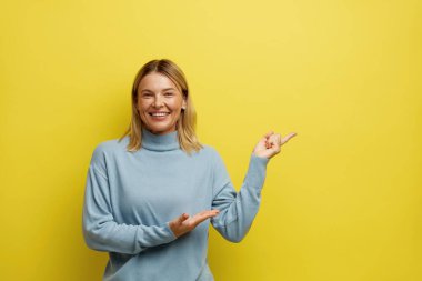 Yanını gösteren mutlu kadın. Genç Kız Boş Kopya Uzayı 'nı göstererek eğleniyor. Güzel Dişi Gülümseyen Dişi, Sarıda soyutlanmış. Reklam Kavramı 