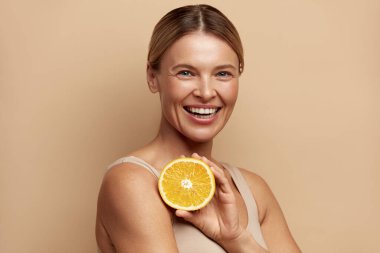 Portakal Meyveli Gülümseyen Güzel Kadın. Işıl ışıl yüz derisi ve turuncu portresi olan pozitif kadın. Doğal makyajlı ve parlayan nemli ciltli kız mankeni. C vitamini kozmetik kavramı 