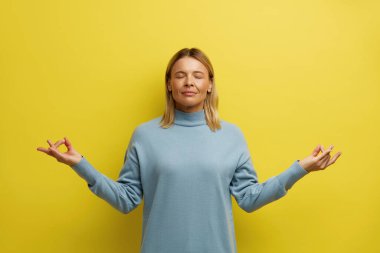 Huzurlu Kadın Stüdyoda Meditasyon. Çekici Genç Kızın Portresi Rahatlıyor ve Parmaklarıyla Meditasyon Yapıyor, Yoga Çalışıyor. Kapalı Stüdyo Çekimi Sarı Arkaplanda İzole Edildi 