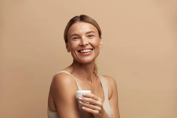Beauty Woman Holding Face Cream. Closeup Of Female Model With Fresh Skin Laughing with Cream Bottle In Hand. Skincare Concept. High Resolution