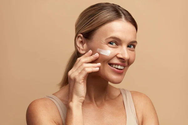 Positive Woman Applying Face Cream. Closeup Of Female Model With Fresh Skin Applying Cosmetic Product Under Eyes. Skincare Concept. High Resolution
