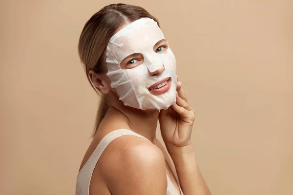 Beauty Woman Face Mask. Portrait Of Beautiful Girl Posing in White Sheet Mask at Healthy Fresh Skin. Closeup Of Attractive Woman With Natural Makeup And Mask On Facial Skin. High Resolution