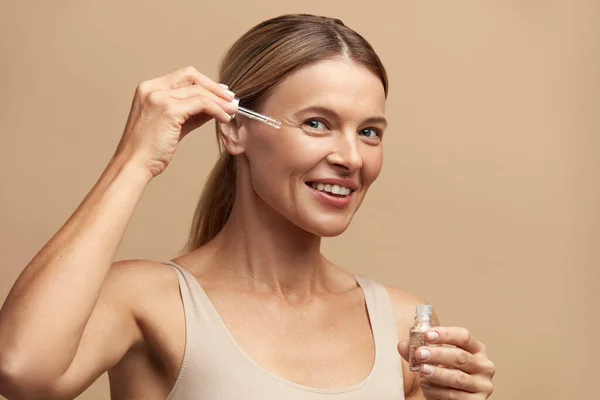 Woman Applying Serum on Face. Woman Applying Essential Oil On Facial Skin And Looking at Camera. Beautiful Model Moisturizing Derma With Natural Vitamin E, Serum Collagen And Hyaluronic Acid