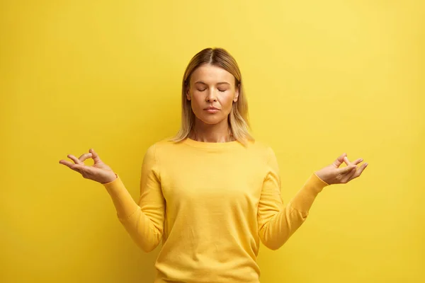 スタジオで瞑想する平和的な女性 魅力的な若い女の子の肖像指でリラックスして瞑想ジェスチャーを行う ヨガを練習 黄色の背景に隔離された屋内スタジオショット — ストック写真