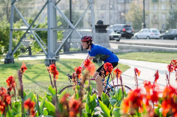 Hombre de uniforme azul en la bicicleta de carreras cerca de las flores de Canna — Foto de Stock