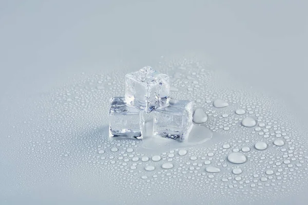 Three ice cubes with drops of water on a gray background — ストック写真