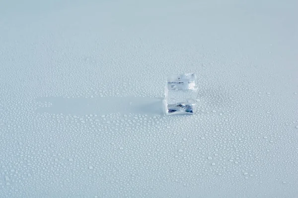 An ice cube glides across a gray background in drops of meltwater — Photo