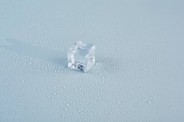 one ice cube on a gray background close-up, behind it is left a trace on the background