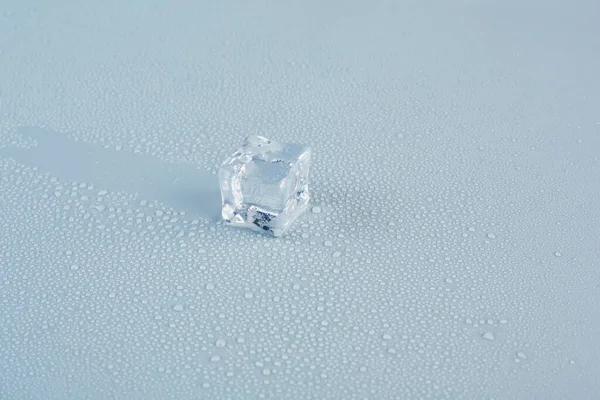 One ice cube on a gray background close-up, behind it is left a trace on the background — Photo
