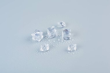 A lot of ice of different sizes on a gray background in water droplets