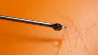 Şırınga iğnesine aşı düşüşünü yakından çek. Şırıngadan düşen su damlası.