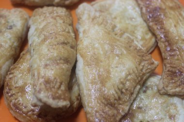 Lezzetli ev yapımı baharatlı ve çıtır çıtır samosa hamur tatlısı ahşap zemindeki beyaz seramik tabağa yerleştirilmiş.