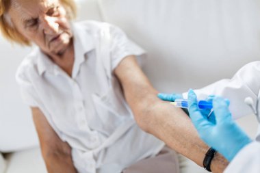 Doktor yaşlı bir hastaya aşı uyguluyor.