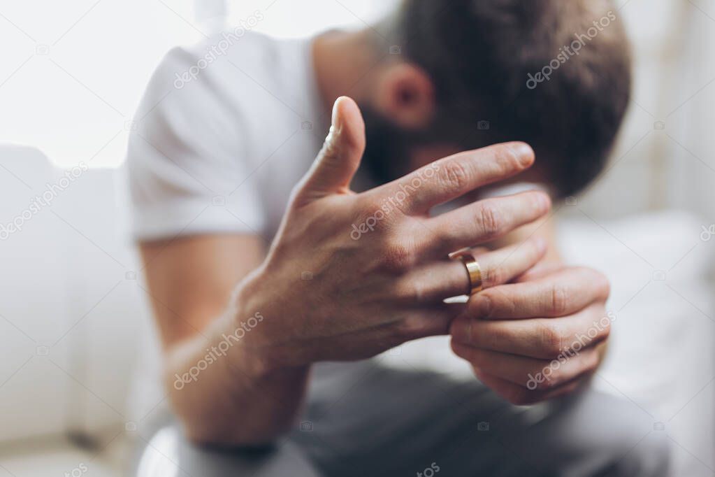 Heartbroken man at home holding a wedding ring