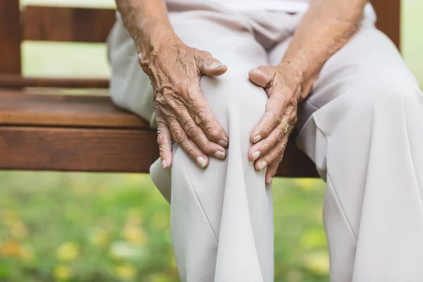 老妇人坐在长椅上 抱着疼痛的膝盖 图库图片