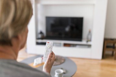 Uzaktan kumandalı yaşlı kadın televizyon izliyor.