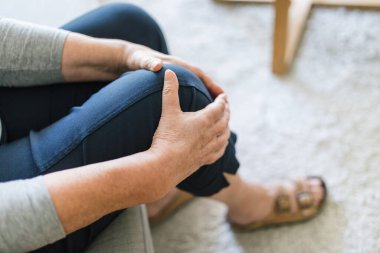 Senior woman sitting on bench, holding her painful knee