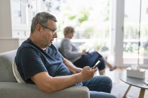 上了年纪的夫妻坐在沙发上 在家里用手机 — 图库照片