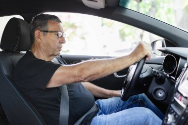 Happy senior in his 70s driving a car