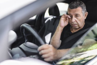 Tired pensioner in his 70s, dring in a car