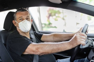 Senior in his 70s driving a car wearing face mask for protection against corona virus