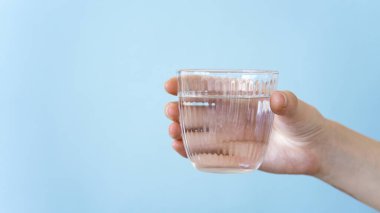 Şeffaf bir bardak su tutan kadın eller. Sağlıklı bir yaşam tarzı. mavi arkaplan.