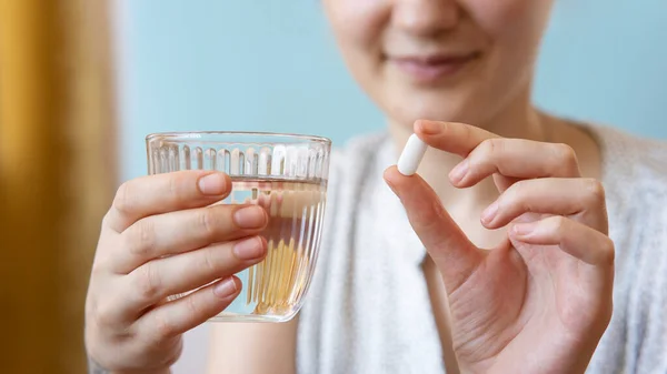 Close up woman holding pill in hand with water. Female going to take tablet from headache, painkiller, medication drinking clear water from glass. Healthcare, medicine, treatment, therapy concept
