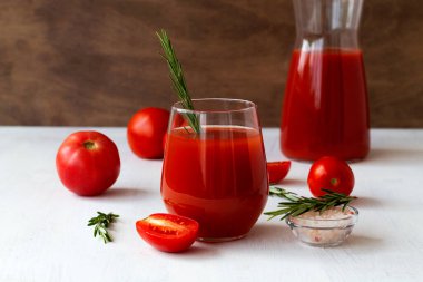 Beyaz üzerine kırmızı domates suyu ve taze domates. Yeşil biberiyeli bir bardaktaki domates suyu beyaz arka plan fotokopi alanında izole edilmiş..